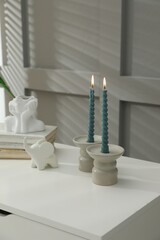 Candlesticks with burning candles on table near grey wall
