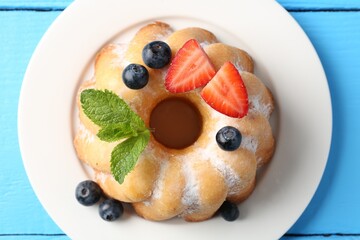 Tasty Bundt cake with powdered sugar and berries on light blue wooden table, top view