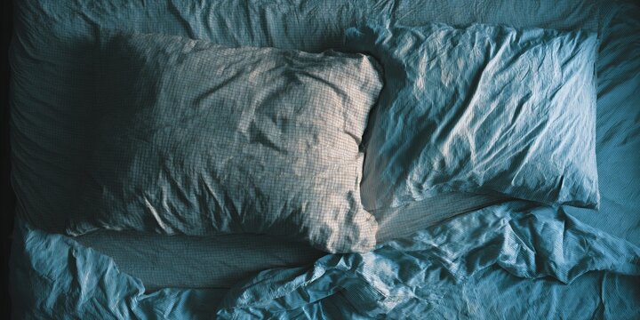 Comfortable unmade bed with rumpled sheets and pillows in soft morning light