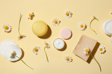 Different chamomile cosmetic products with cotton pads and flowers on yellow background