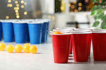Orange ball falling into plastic cup on light table against blurred lights, closeup. Beer pong game