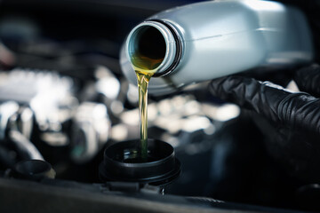 Worker pouring motor oil from canister into car engine, closeup