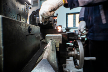 Close up view of a factory worker operating heavy industrial machinery with focus on precision. Gloved hands adjust the controls in a mechanical workshop, emphasizing safety, expertise, and metalwork.