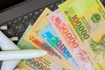 Vietnamese dong cash currency rests on laptop keyboard beside small airplane model, hinting at travel plans.