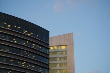 Modern office buildings with glass and tiled facades illuminated in the early evening under a clear sky
