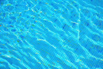 Close-up view of water ripples and reflections in a bright blue swimming pool with tiled bottom creating light patterns