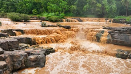 Floodwaters laden with sediment flow forcefully through a rocky terrain, highlighting the...