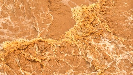 Drone aerial view of turbulent, sediment-laden floodwaters crashing over rocks, illustrating the...