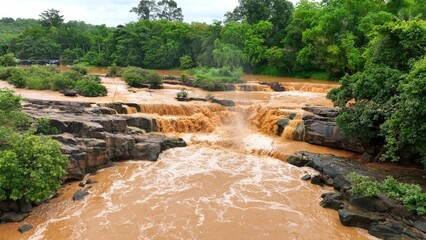 Aerial drone view of muddy floodwaters surging through river rocks, illustrating natural disaster...
