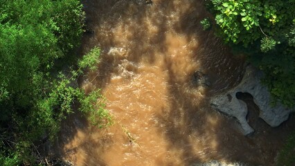 From above, a drone reveals fast-moving floodwaters in a thriving rainforest, illustrating the...