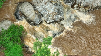 Aerial perspective captures fast-flowing river water surrounded by rich forest greenery, illustrating the vitality and movement within an untouched natural environment. Thailand.
