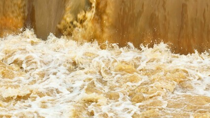Drone aerial perspective shows sediment-filled water rushing forcefully over a natural edge, emphasizing the continuous cycle of erosion and renewal in river landscapes.
