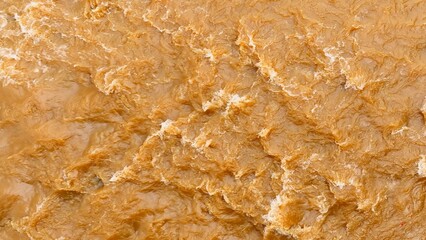 Aerial view shows brown floodwater turbulence, showcasing floodwaters rich in sediment that shape riverbanks and contribute to soil fertility during natural flooding.

