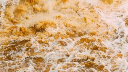 Drone perspective of swirling muddy floodwaters, emphasizing the powerful flow and sediment movement typical of flood events affecting ecosystems and terrain.
