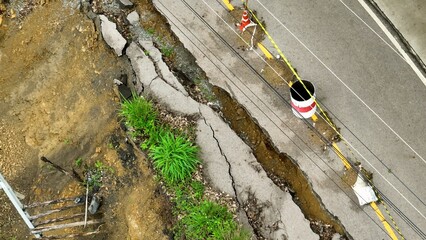 Drone view displays road collapse and earth displacement caused by flooding and heavy rain, emphasizing the hazards faced in mountainous or forested areas during storms. Thailand.
