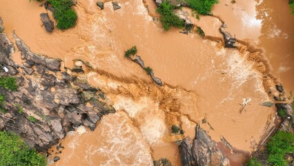 Bird’s eye shot captures turbulent floodwaters cascading through rocky terrain, highlighting the increased frequency of flooding due to climate change and rising global temperatures. Thailand.
