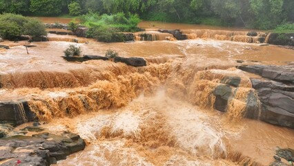 Bird’s eye shot captures turbulent muddy waters cascading through a rocky river, emphasizing floods exacerbated by human activities such as deforestation and poor land use. Thailand.
