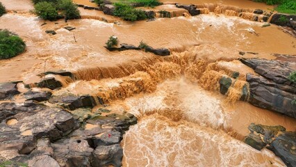 Drone aerial view of sediment-laden floodwaters rushing over rocks, illustrating the severe flooding worsened by deforestation and land mismanagement, highlighting human impact on natural disasters.
