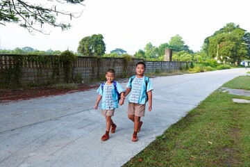 Two siblings in uniform walk to school.