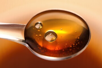 Close-up of a silver spoon filled with golden amber liquid with tiny bubbles reflecting warm light