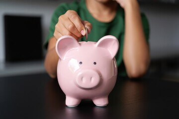 person inserting a coin into a pink piggy bank symbolizing saving money with focus on the piggy bank and hand