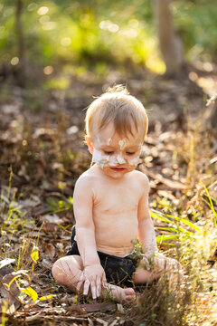Portrait of aboriginal baby boy with ochre on face and feeding tube sitting in bushland