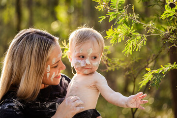 Portrait of Aboriginal mum holding baby boy faces painted in ochre in Australian bushland