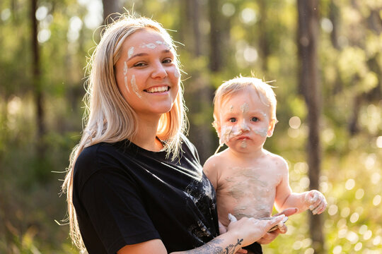 First Nations Australian woman with baby boy applying cultural ochre body paint mixed in shell
