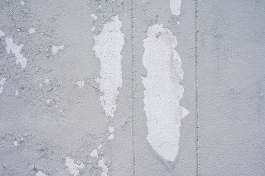 Peeling paint on gray concrete wall. Peeling, cracking, or blistering paint occurs when there is a loss of adhesion between the paint and the surface it's placed on.