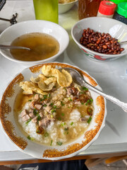 Hearty rice porridge with savory beef broth, topped with crispy crackers and peanuts, a beloved breakfast dish commonly enjoyed in Pontianak and Singkawang. Bubur Kuah Daging.