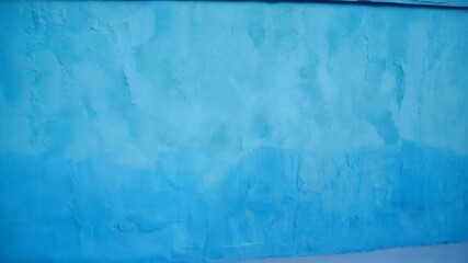 Close-up of textured blue wall, showcasing various shades, slight imperfections, and an abstract pattern painted with a paintbrush strokes.