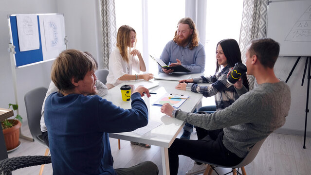 The happy advertising team smiles at the meeting. A group of beautiful young people are sitting at a table in a family office