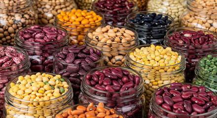 Assorted colorful dried beans, including kidney, pinto, black-eyed peas, and lentils are displayed in glass jars for storage.