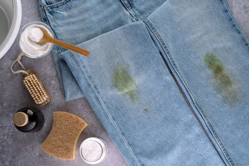 Dirty jeans with grass on their knees are ready for home stain removal. Cleaning supplies such as a...