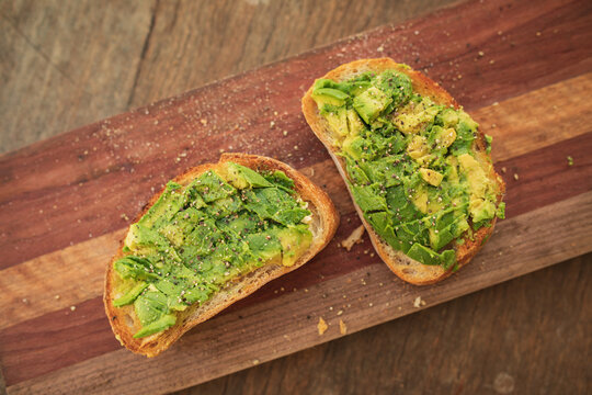 Smashed avocado on toast with salt and pepper on wooden board
