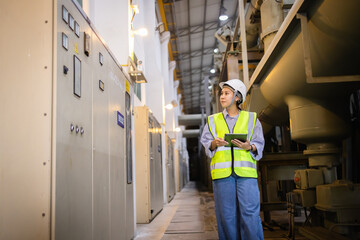 Engineer inspects electric grid field using tablet near insulated gas switchgear equipment in large...