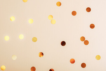 Golden confetti scattered on a soft beige background, texture