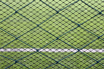 Fototapeta premium Close-up of a green sports net fence with a blurry football field in the background. Ideal for illustrating boundaries, protection, or sports facilities.