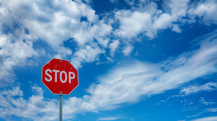 Red stop sign standing tall under a vibrant blue sky with scattered white clouds