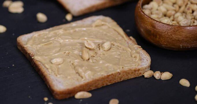 wheat bread with bran and soft peanut butter, peanut butter on a piece of bread and roasted peanuts on the table, close up