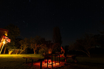 Woman sitting by backyard fire pit looking up at the stars in the night sky above