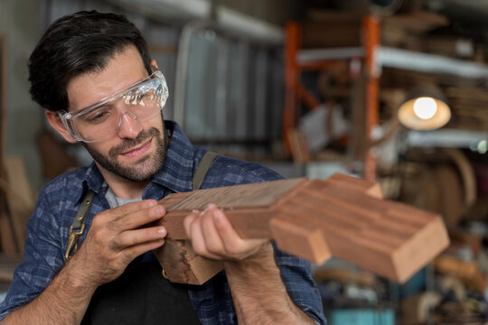 Focused male carpenter inspecting wooden guitar neck in workshop, wearing safety goggles for woodworking precision - Powered by Adobe