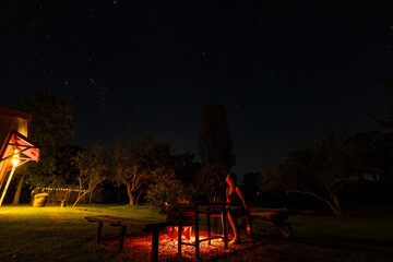 Woman sitting by backyard fire pit looking up at the stars in the night sky above