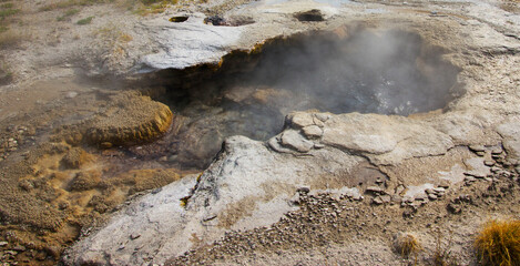 Steam erupts from a geothermal hot spring in Yellowstone national park, showcasing the intricate landscape and mineral formations
