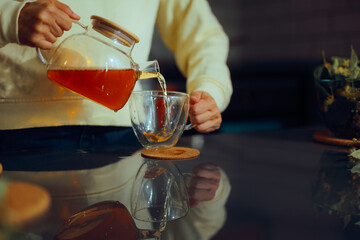 Person Pours Herbal Tea from a Teapot into a Teacup. Woman preparing a natural herbal drink