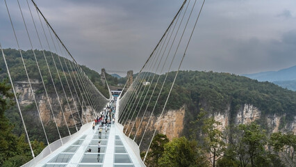 A unique glass bridge over the gorge. People are walking on a transparent surface. The support...