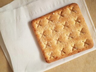 A square cracker on white paper. A popular and simple snack.