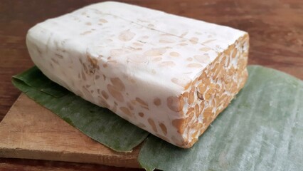 Fresh tempeh bars made from soybeans wrapped in banana leaves on wooden table. 