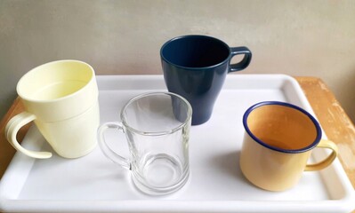 A collection of different mugs made of different materials on a white tray.