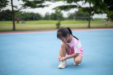 A young girl is kneeling on a blue court, wearing a pink shirt and shorts.